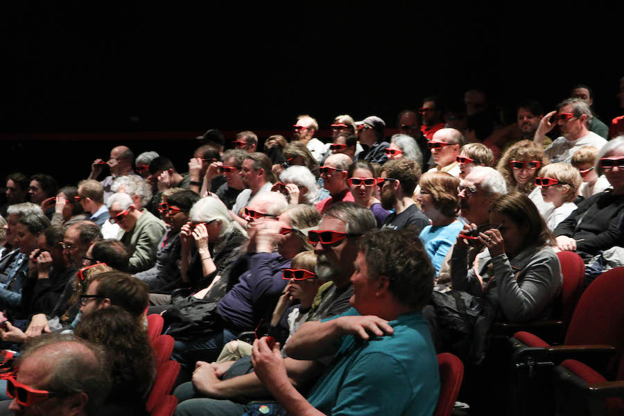 Audience seated in auditorium theater wearing red plastic 3D glasses